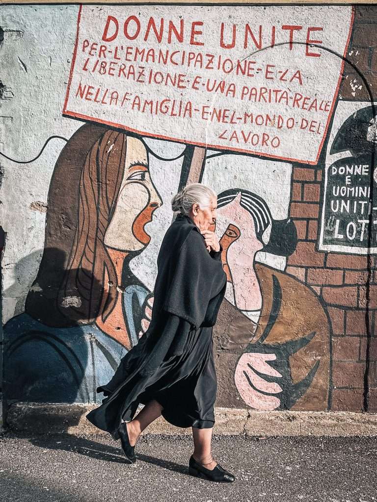 signora di fronte a murales di orgosolo